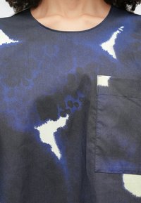 Tengerészkék ing absztrakt kék és fehér mintákkal, mellzsebbel és kerek nyakkivágással. Sima anyag enyhe fényességgel.