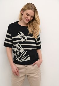 Stribet sweater i sort og creme med blomstermotiv, korte ærmer og rund halsudskæring. Bærers sammen med lysebeige bukser med knapdetalje.
