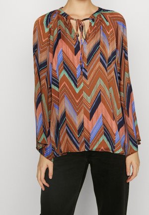 Blusa multicolore con un motivo a zig-zag in marrone, blu navy e colori pastello, con scollatura a fiocco e maniche lunghe.