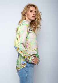 Zijde blouse met een lichtbeige achtergrond, versierd met kleurrijke bloem- en bladerpatronen. Lange mouwen, licht gebogen onderkant en levendige accenten.