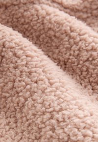 Gros plan sur un tissu polaire doux beige avec une surface texturée, duveteuse et des fibres étroitement enroulées.