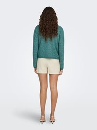 Turquoise knit sweater with a relaxed fit, paired with cream shorts. The sweater has long sleeves and a rounded hem. White heeled sandals.