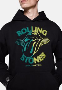 Czarna bluza z kapturem z żywą grafiką przedstawiającą język i skrzydła. Napis zawiera "ROLLING STONES" oraz "FORMULA ONE TEAM" w kolorze żółtym i turkusowym.