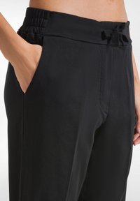 Zwarte relaxte broek met een elastische tailleband, gestrikte strikdetail en zijzakken, gemaakt van een gladde, lichtgewicht stof.