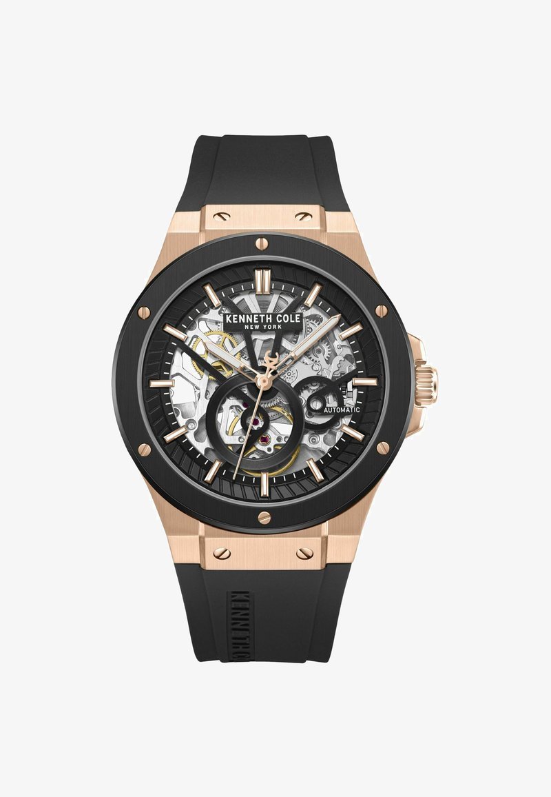 Zwarte automatische horloge met een transparante skeleton wijzerplaat, rubberen band en roségouden accenten op de kast en uurmarkeringen.