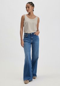 Top beige senza maniche abbinato a jeans a vita alta in denim azzurro chiaro a gamba larga. I jeans presentano un classico design a cinque tasche e una leggera scoloritura.
