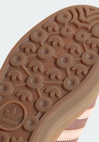 Semelle en caoutchouc brun de basket avec des motifs de traction circulaires et en forme de feuille, présentant un logo adidas en relief dans un design circulaire.