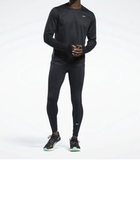 Svart fukttransporterande långärmad tröja och tights med en smidig struktur, tillsammans med svarta och flerfärgade löparskor.