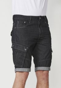 Schwarze Denim-Cargo-Shorts mit aufgerollten Säumen, ausgestattet mit mehreren Taschen, Stickdetails und einem Knopfverschluss.