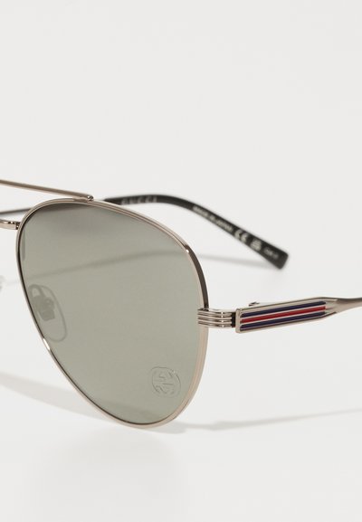 Aviator sunglasses with metal frame, grey lenses, and black arms featuring multicolored striped accents. Logo embossed on the lens.
