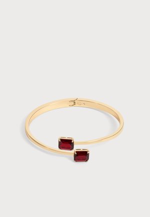 Bracelet jonc ouvert en or avec deux pierres précieuses rouge profond taillées en carré à chaque extrémité sur un fond clair.