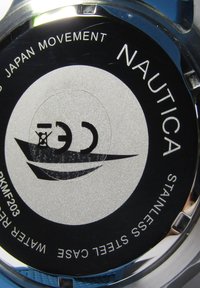 Ümmargune Nautica kell, millel on roostevabast terasest korpus, must ja hõbedane värvilahendus, Jaapani liikumise tekst ja paadi logo detail.