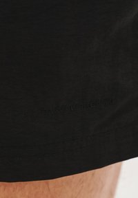 Czarne szorty o gładkiej fakturze, delikatnym wzorze, przeszytych brzegach i wytłoczonym napisie "PARK LORENTE" po dolnej stronie.