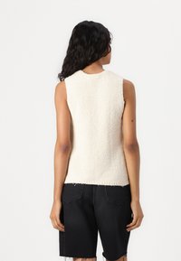 Top sans manches en crème texturé avec une finition douce, présentant un col rond et un ourlet brut, associé à un short en denim noir.