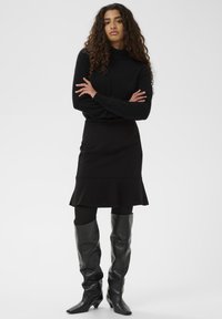 Black turtleneck sweater, fitted black flared skirt, and knee-high leather boots with pointed toes. Smooth textures with a monochromatic palette.