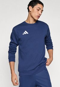 Φούτερ σε σκούρο μπλε ναυτικό χρώμα, κατασκευασμένο από μαλακό ύφασμα, με στρογγυλή λαιμόκοψη και ριμπ μανσέτες. Φέρει λευκό λογότυπο Adidas στο στήθος.