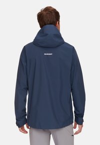Giacca impermeabile blu navy con cappuccio, caratterizzata da un logo bianco sulla parte posteriore, maniche lunghe e polsini regolabili. Realizzata in materiale impermeabile.