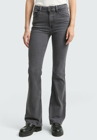 Jeans gris évasés en denim avec une taille haute, dotés de poches avant et d'un léger dégradé. Associés à des chaussures à plateforme noires.