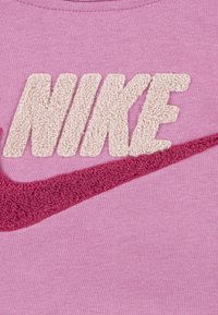Ružová bavlnená mikina so štruktúrovaným krémovým logom "NIKE" a tmavoružovým dizajnom Swoosh. Mäkka, hladká textúra látky.