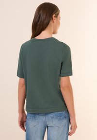 T-shirt vert à manches courtes avec un col rond, texture douce et coupe décontractée, associé à un jean en denim bleu.