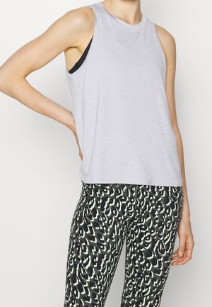 Persoon draagt een mouwloze lichtgrijze top met een zwarte sportbeha zichtbaar en zwart-witte legging met luipaardprint en een hoge taille.