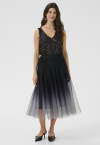 Čierny top s flitrami a výstrihom do V, spárovaný s dlhou, vrstvenou tylovou sukňou ombre s malými trblietkami. Model má obuté špicaté čierne lodičky.