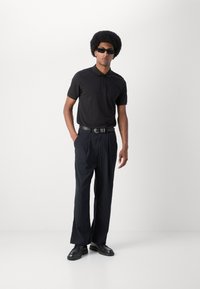 Svart polo-skjorte, mørke stripete bukser, svart belte og sko. Slim fit, teksturert stoff og rette bukser med skreddersydd silhuett.