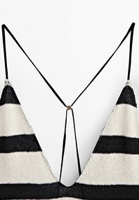 Top en maille rayé de couleur noir et crème, présentant un design en V, des fines bretelles et un accent métallique décoratif à l'arrière.