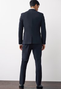 Námořnický oblek s přizpůsobeným střihem. Sako má jeden roz slit a klopové límce. Kalhoty jsou slim fit s jemným skladem. Doplňují ho černé boty.