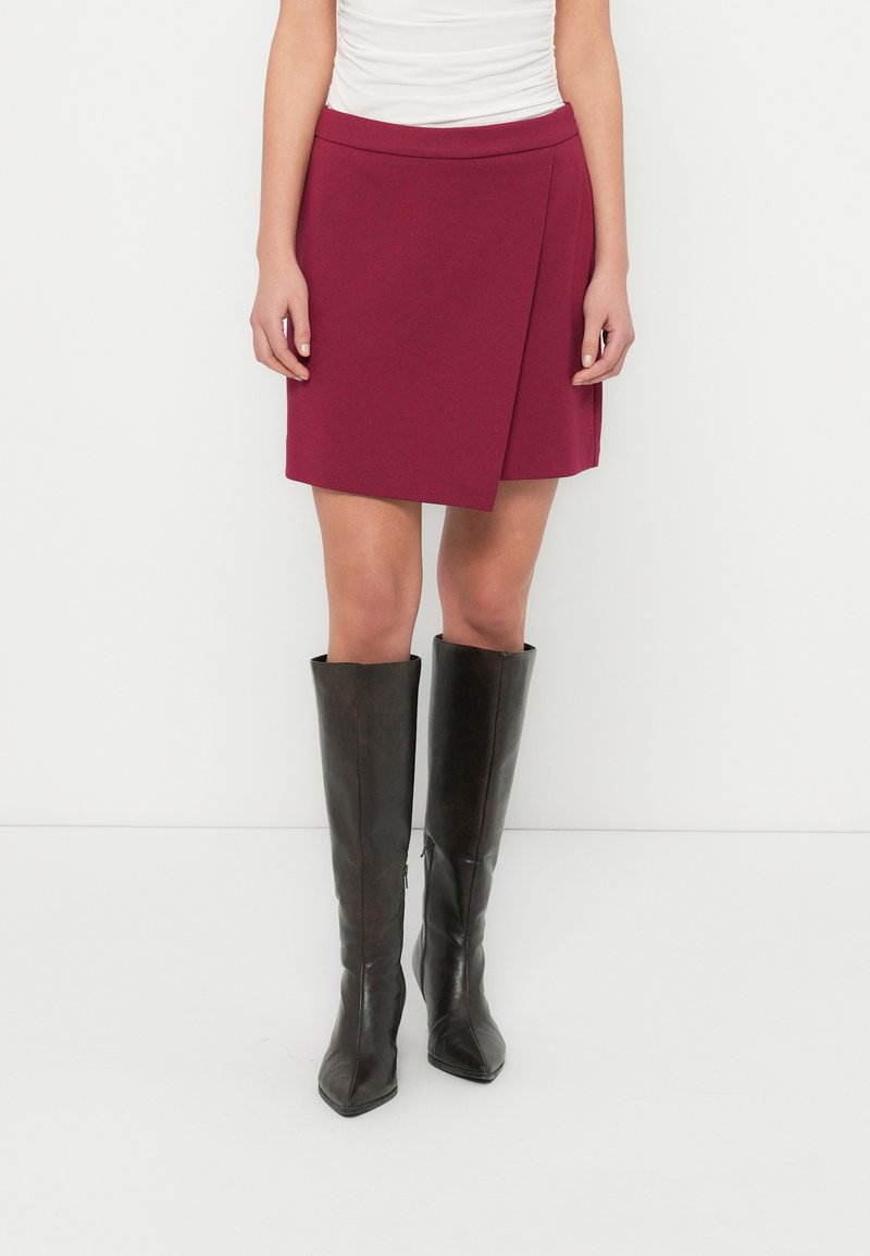 Φούστα σε μπορντό χρώμα με λεία υφή, διαθέτει εφαρμοστή μέση και διαγώνιο τελείωμα. Συνδυάζεται με δερμάτινες μπότες σκούρου καφέ που φτάνουν μέχρι το γόνατο.