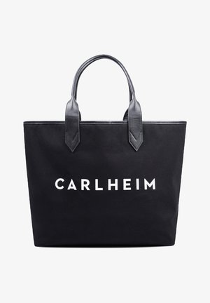 Musta kangaskassi nahkahihnoilla, edessä valkoisilla isoilla kirjaimilla painettu "CARLHEIM".