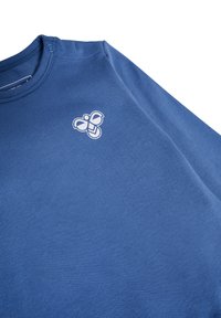 Blå bomullströja med rund halsringning och en vit bi-logotyp på vänster bröst, som visar en slät och jämn textur.