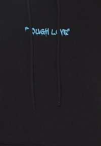 Haut à capuche noir avec un texte bleu dégoulinant qui dit "TOUGH LOVE", avec deux cordons de serrage pour l'ajustement et une texture douce.