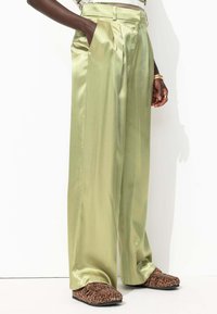Pantalons larges en satin vert clair avec plis en boîte et poches latérales, associés à des chaussures à enfiler à imprimé animal marron.