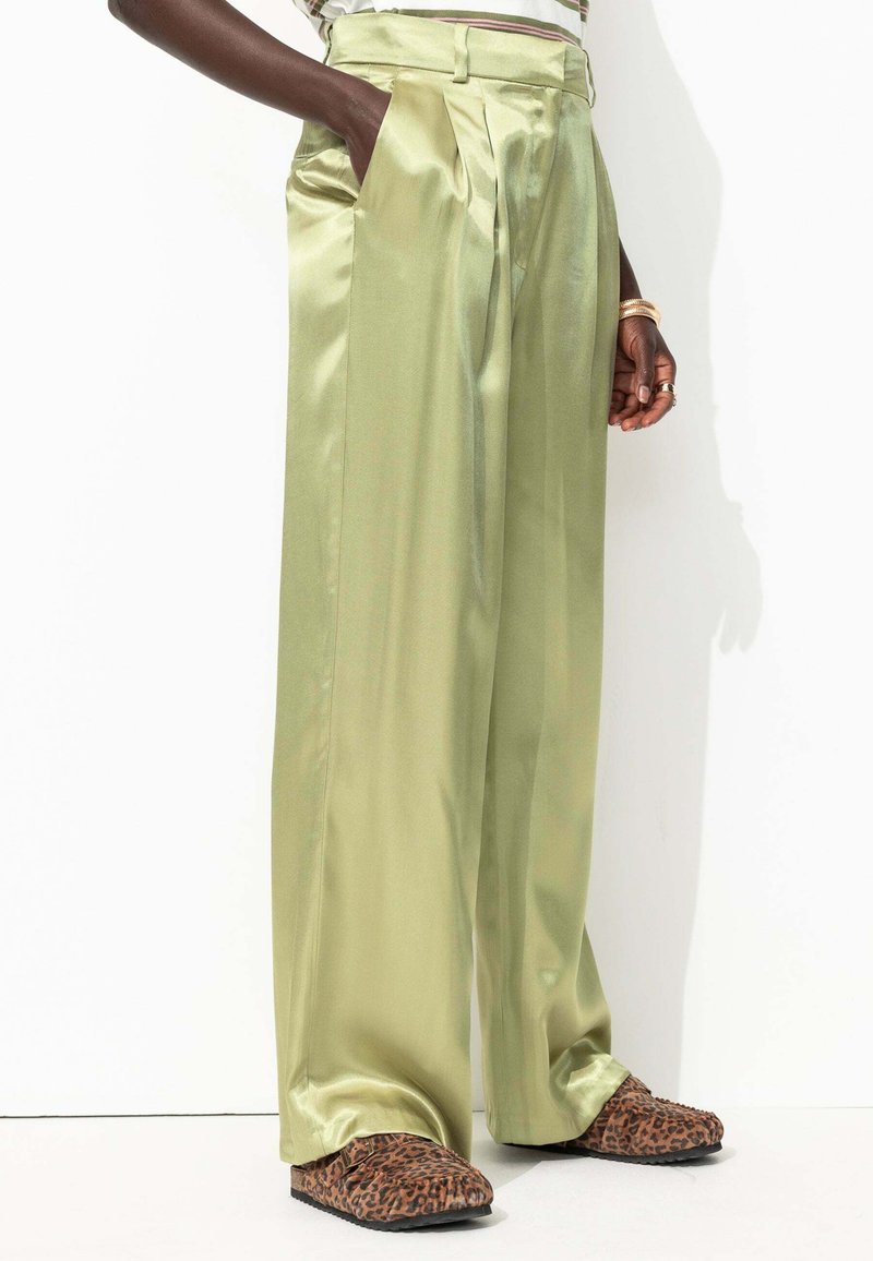 Pantalons larges en satin vert clair avec plis en boîte et poches latérales, associés à des chaussures à enfiler à imprimé animal marron.