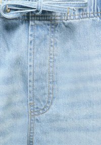Lyseblå denimstoff med synlige sømmer på fremre lomme og et knytt denimbelte i midjen.