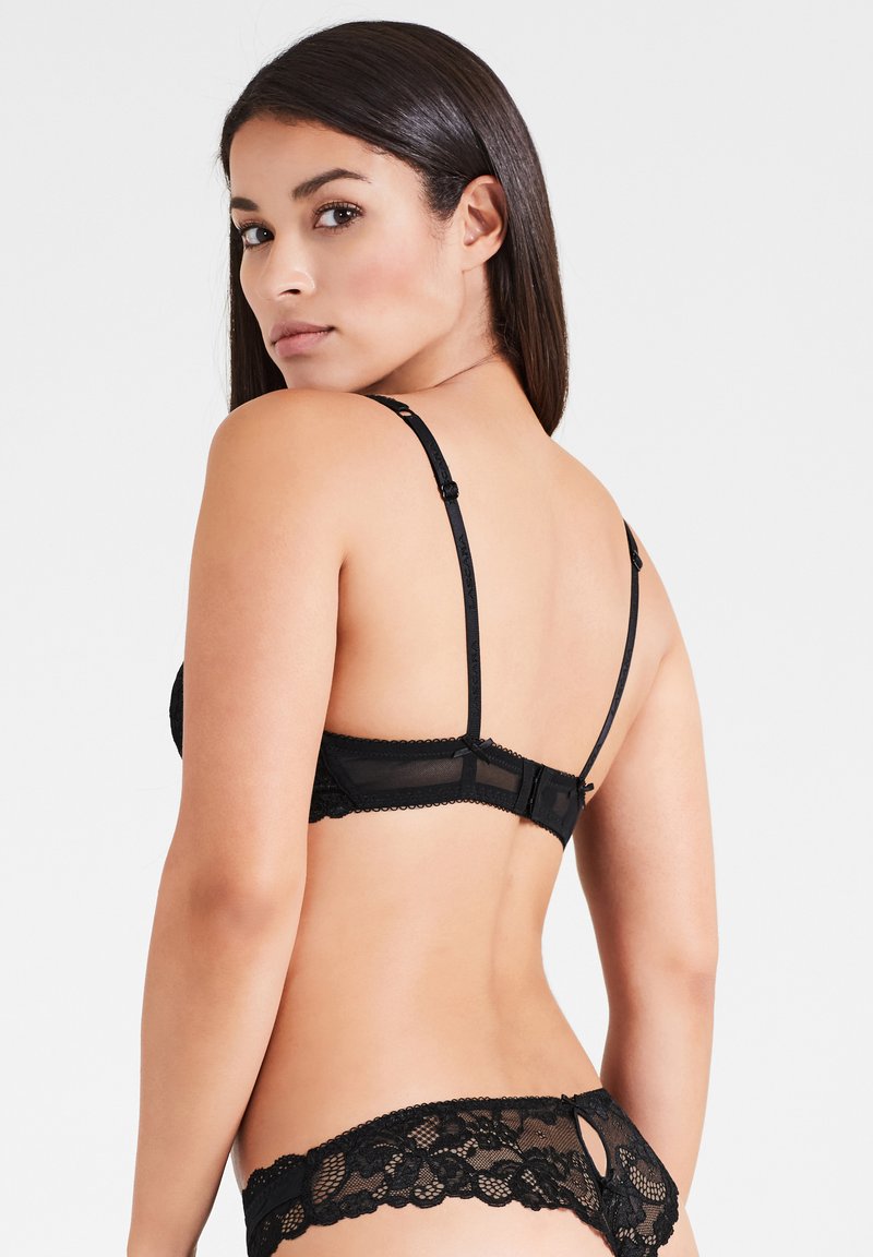 Zwarte kanten lingerieset met een bh met verstelbare bandjes en haaksluiting, vergezeld van een bijpassende slip met bloemenpatronen en uitsnijding.