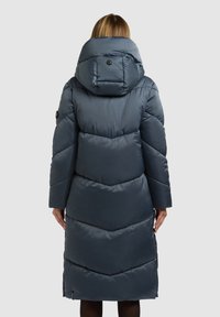 Tumesinine pikk puffer-jope kõrge krae ja üle suurte kapuutsiga. Omab seelikuõmblust ja küljetaskuid. Sile, läikiv tekstuur.