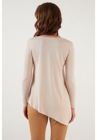 Maglietta a maniche lunghe beige chiaro con orlo asimmetrico, texture morbida e scollatura arrotondata, abbinata a pantaloni beige aderenti.