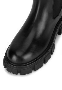 Czarny skórzany botek za kostkę o gładkim wykończeniu, z elastycznymi panelami bocznymi oraz solidną gumową podeszwą z wyraźnym bieżnikiem zapewniającym przyczepność.