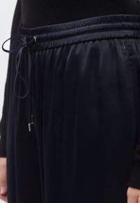 Tumši zilas, vieglas bikses ar elastīgu jostasvietu un aukliņu. Gluda tekstūra, krokaina dizains un sānu kabatas.