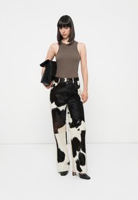 Pantalons en fausse fourrure avec un imprimé vache noir et blanc, associés à un débardeur marron et une pochette noire. Texture lisse, design à jambe large.