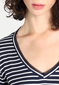 Top a righe navy e bianche con scollatura a V e maniche corte. Tessuto morbido con un delicato bordo nero attorno al collo.