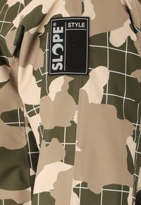 Kamuflage mønstret stof i beige og grøn med et gitteroverlay; indeholder et sort "SLOPE STYLE" label, der er præsenteret tydeligt.