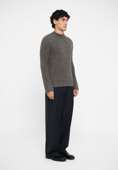 Gray knit sweater with a round neckline, worn with dark pinstripe trousers and black shoes. Fabric appears soft and textured.