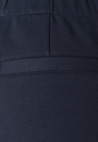 Laikku sininen venyvä kangas, jossa on sileä rakenne, vaakasaumadetalji ja joustava vyötärö, joka tarjoaa mukavuutta ja istuvuutta.