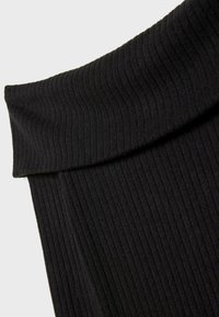 Gros plan sur un tissu côtelé noir avec un col roulé replié sur un vêtement tricoté.