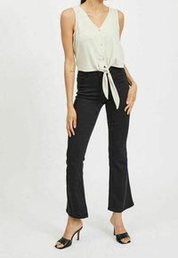 Light gray sleeveless top with a v-neck and front tie, paired with high-waisted black flared jeans and open-toe black heels.