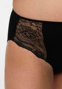 Melnas apakšbikses ar mežģīņu paneļu sānos, gludu melnu audumu un sarežģītu mežģīņu dizainu ar ziedu rakstu.