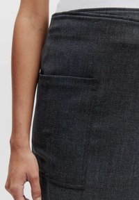 Donkergrijze denim rok met een voorzak, een vlakke tailleband en een gladde textuur. Close-up weergave van de stofdetails van de rok.